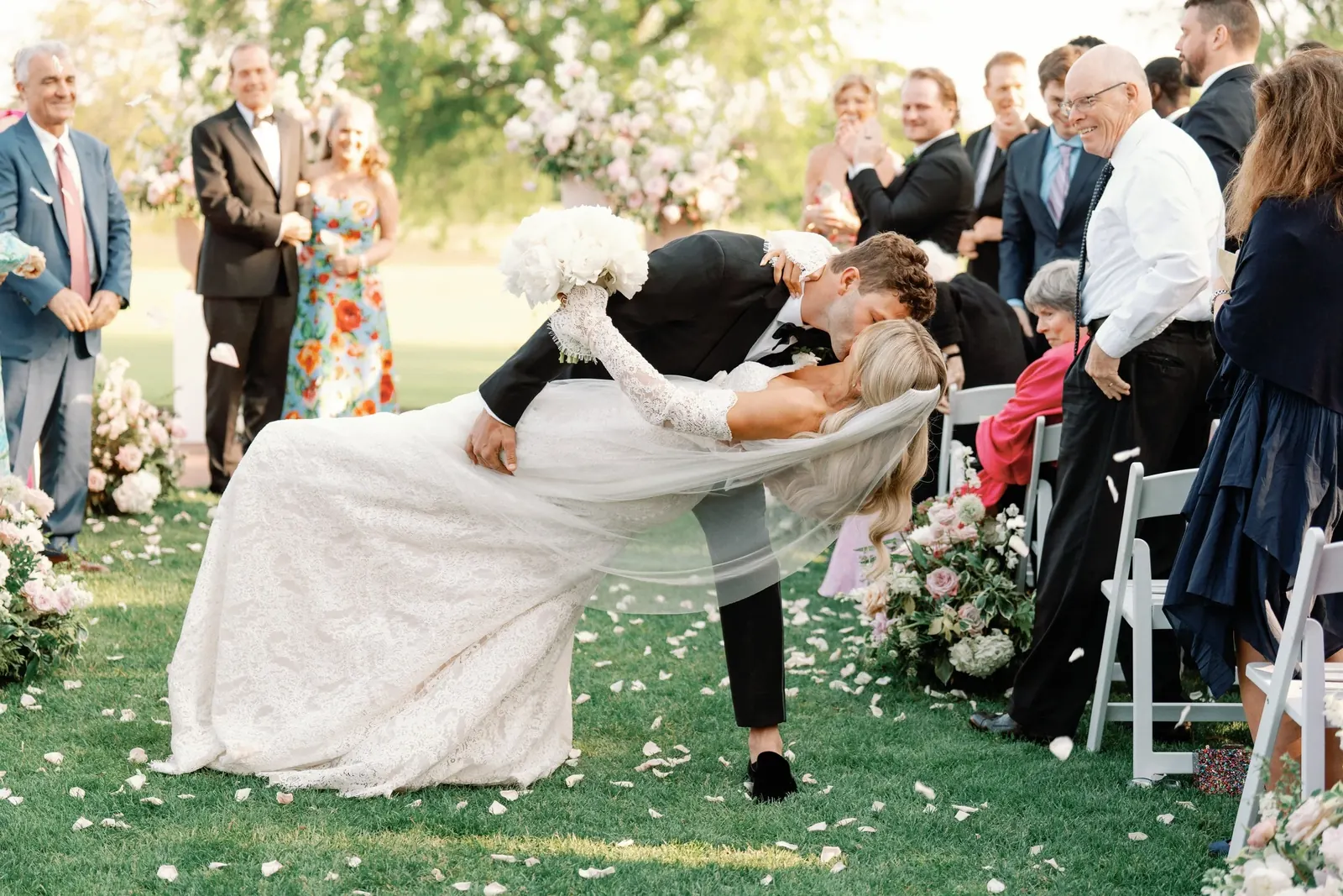 A groom dipping his bride for a kiss as guests cheer