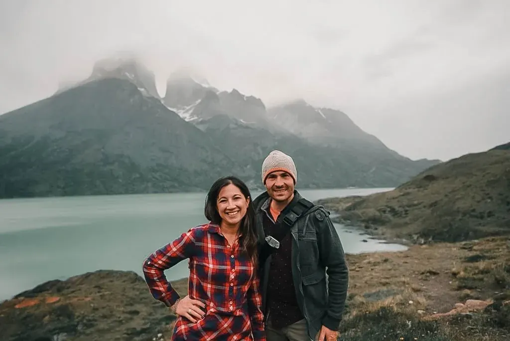 Dan and Lydia smiling in front of jagged mountain peaks and a lake