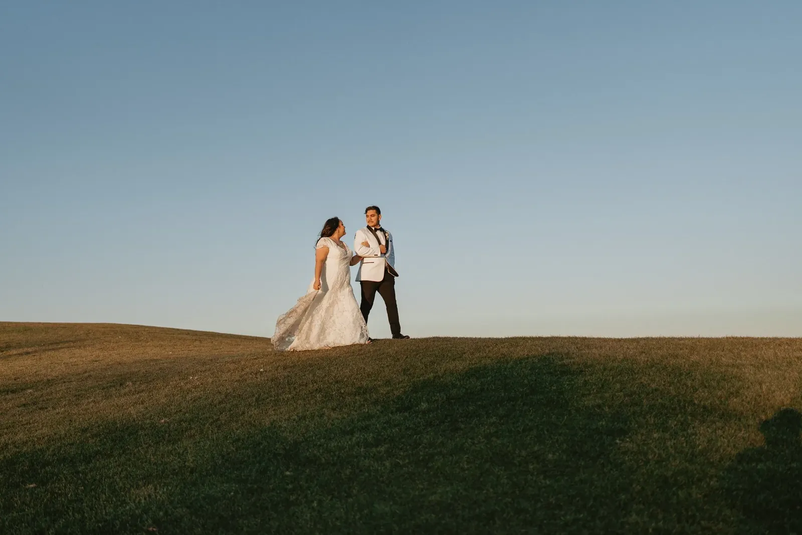 Manny and Karina walking across an open field at sunset