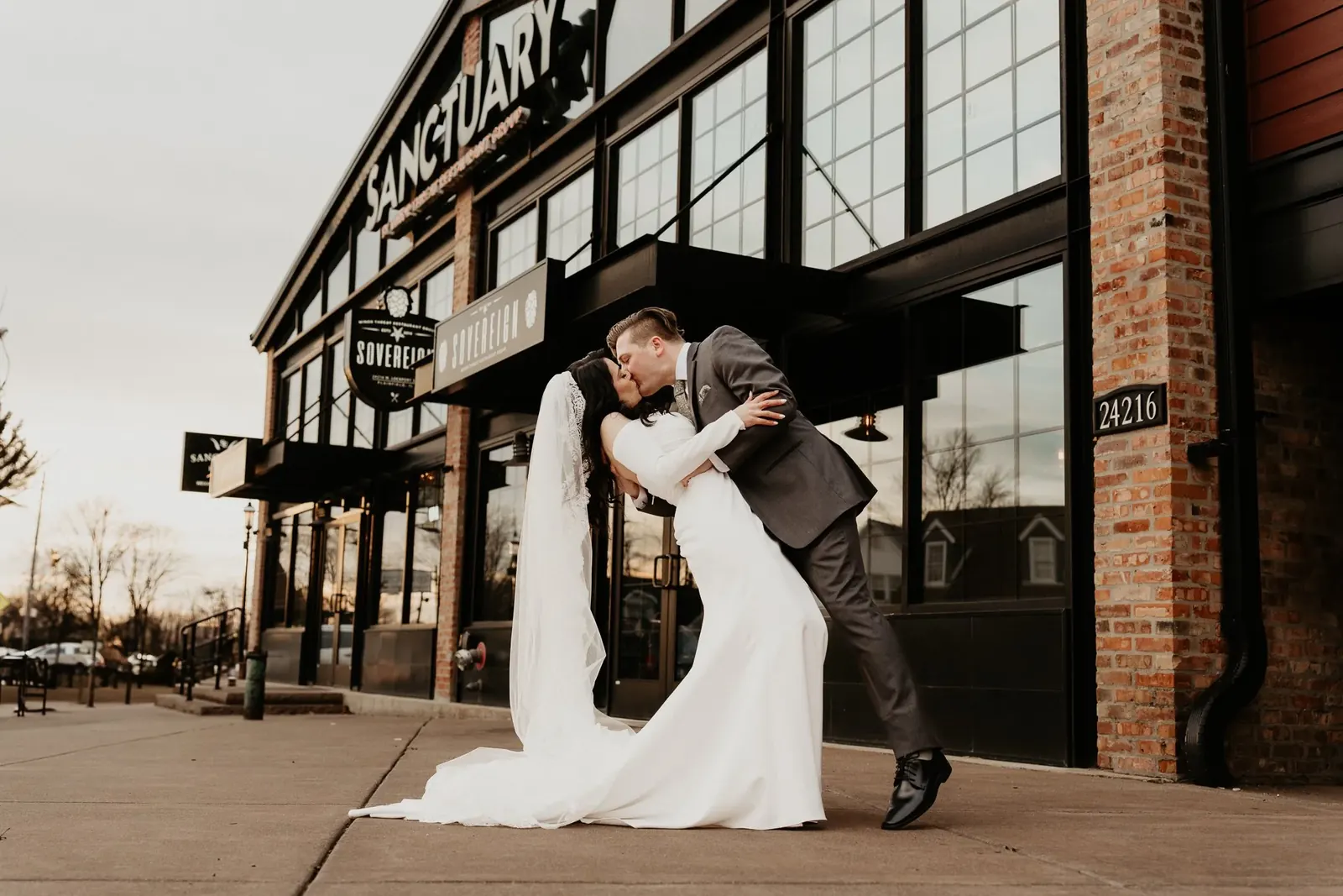 A groom dipping his bride for a kiss outside a brick venue